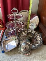 Photo showing the full seven-piece silver plated set, including the three-tier server, various trays, and covered dish placed on floor against red curtain and wooden surface.