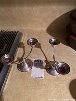 Two sterling silver dual-arm candle holders on a beige surface, with tarnish visible