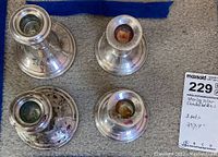 Four sterling silver candleholders shown upside down, visible dark tarnish spots. Two sets of two candleholders each, different weights and designs.