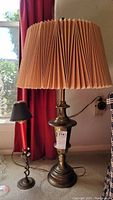 Full view of the 33-inch Stiffel brass lamp with damaged beige pleated fabric shade, and 9-inch red and black metal candle holder on the left.