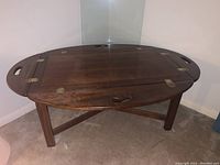 Wooden oval table with glass inset top, fold down sides with brass hinges and cutout handles, placed in corner against walls