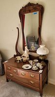 Full view of vintage wooden chest with drawers and mirror, showing overall shape, attached mirror, and decorative items on top.