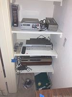 Full view of shelving with Sony and Emerson vintage electronics including Betamax player, VHS recorder, remotes, and power adapter.