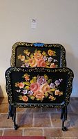 Two stacked vintage metal trays with floral designs on black background with gold detailing.