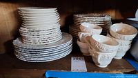 Full shelf view showing stacks of Wedgwood embossed white plates in large, medium, and small sizes, with a row of embossed teacups in front.
