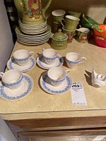 Five white Wedgwood tea cups and four matching saucers arranged on countertop, one white cup shows a break visible on top right corner