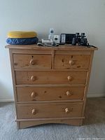 Front view of five-drawer wood chest showing natural wood finish with wooden knobs and surface wear.