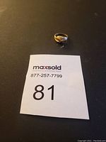 Image showing the 14k gold ring placed on a black surface next to a MaxSold label number 81.