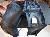 Two pairs of blue denim jeans laid flat on a dark surface; one pair marked with size 33 tag.