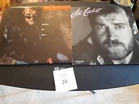 Photo showing two Joe Cocker vinyl albums, 'Unchain My Heart' and 'Civilized Man', laid side by side on a black surface with a lot number card.