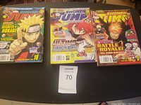 Photo showing three Shonen Jump comic books side by side on a black surface with a lot number card in front.