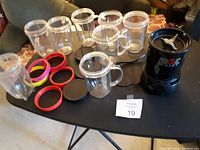 Black Magic Bullet blender base with blade attachment, surrounded by multiple clear plastic blending cups, black and colorful lids on a black table.