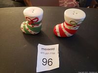 Two ceramic Christmas stocking salt shakers displayed side by side on a black surface, showing decorative bows and holes on the top.