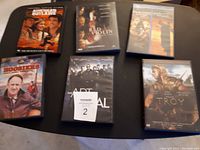 Photo showing six DVD cases arranged on a dark surface: Hoosiers, The Red Violin, The Patriot, Troy, The Sum of All Fears, and The Last Samurai.