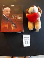 Photo showing The House of Cards Trilogy DVD box set alongside a plush stuffed dog holding a red heart on a dark surface.