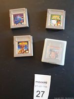 Four original Game Boy cartridges labeled Tetris, Kirby's Dream Land, Metroid II, and Home Alone, plus one empty plastic case, arranged on black surface.