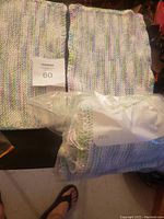 Two handmade knit baby sweaters in pastel multicolor yarn, one laid flat and one packaged, with size 60 tag visible.