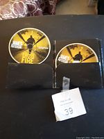 Two Cross Fire audiobook CDs by James Patterson displayed in their black cardboard case. Both discs are labeled and partially inserted in slots called 1 and 2.