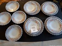 Top view of 10 porcelain plates arranged on a surface, showing floral patterns around the rim in orange and gray colors.