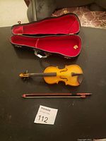 Miniature Villon violin ornament with bow and black hard case open showing red velvet lining, placed on a flat surface alongside a lot card.