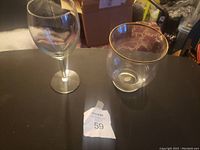 Photo of a clear wine glass with a stem and a clear glass vase with a gold rim on a table.