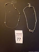 Photo showing two women's necklaces on a dark surface with a MaxSold lot number card.
