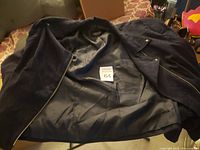 Photo showing the open black women's jacket with visible zipper and lining, placed on a chair.