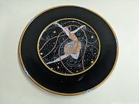 Top view of the black decorative charger plate featuring the ballerina illustration, signature visible