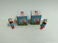 Two Richard Scarry cat character Christmas ornaments with blue pants and red skis, each displayed beside their original boxes.