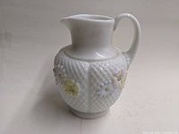 Front angle view of the milk glass pitcher showing textured diamond pattern and painted pastel flowers.