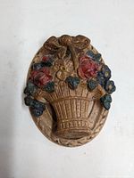 Front view of oval cast iron door knocker with detailed basket of flowers in original painted colors including reds, blues, yellows, and greens.
