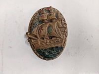 Front view of oval cast iron door knocker showing sailing ship design with original paint and some wear.