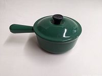 Side angle photo of dark green Le Creuset sauce pan with lid, showing handle and glossy finish.