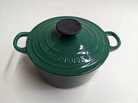 Dark green Le Creuset round Dutch oven with lid, showing exterior with Levy Creuset lettering and black knob.