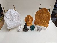 Group photo showing all six Buddha figures and plaques arranged on a table with two large plaques in the back and four smaller items in front.