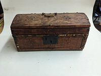 Front view of antique wooden box showing curved lid, brass handle and metal lock plate