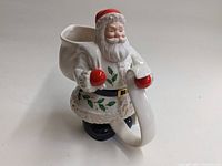Front and angled view of Santa Claus pitcher showing facial detail, holly and berry coat decoration, red hat, scroll shape handle with red gloves.