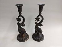 Pair of brass dolphin candlesticks displayed side by side showing overall design and patina.