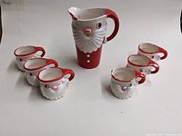 Full set of one pitcher and six mugs arranged side by side on white background