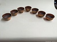 All seven brass and copper decorative bowls arranged in a row showing their shape and size.