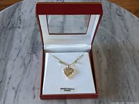 Full view of the sterling silver heart necklace with emerald and diamond accents displayed in a red box with white interior padding.