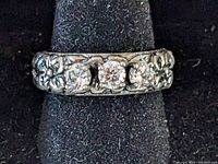 Close-up view of the ring front showing the 3 clear stones and flower band detail on black display