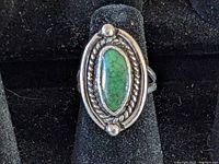 Close-up of the oval turquoise colored stone set in a twisted rope silver bezel with bead accents, mounted on a dark background.