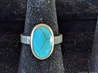 Front view of silver ring with oval turquoise colored stone centered on band, displayed on black ring holder.