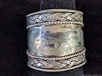 Close-up photo showing front view of wide sterling silver ring with braided edge detail.