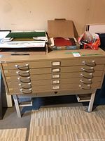 Full view of beige metal flat file cabinet with six drawers and items on top