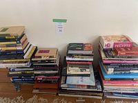 Three stacks of assorted art, travel, language, and culture books on a wooden floor against a white wall