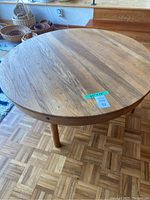 Full view of round wooden coffee table showing table top and legs on parquet floor, with various wooden bowls in background.