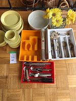 Overview of yellow dishes, cutlery trays with stainless steel cutlery, and glass vases with artificial flowers on wooden floor.