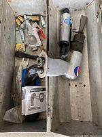 Inside view of metal toolbox showing pneumatic air blow gun, air tool, assorted air fittings, and instruction manual.